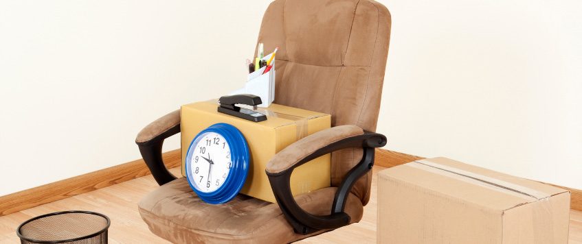 Umzugskarton, Uhr und Büromaterial auf Bürostuhl