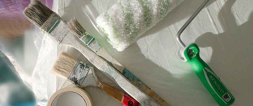 Malerutensilien liegen auf einem weißen Untergrund neben Abdeckfolie