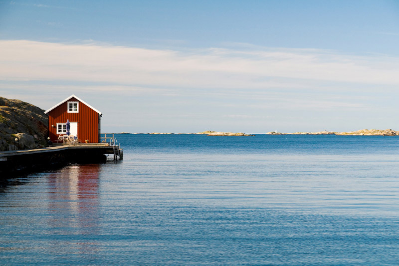 Blick auf eine Hütte im typischen Schweden-Rot an einem weiten See