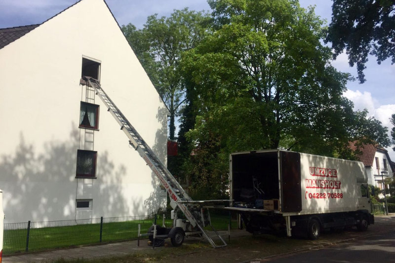 Ein Mansholt Umzugswagen steht vor einem hohen Bürogebäude, an dessen Fassade ein Möbellift nach oben führt.