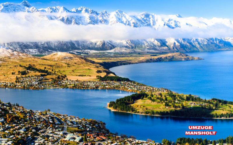 Landschaftsbild von Neuseeland mit Gewässer, Ortschaften und schneebedeckten Bergen im Hintergrund
