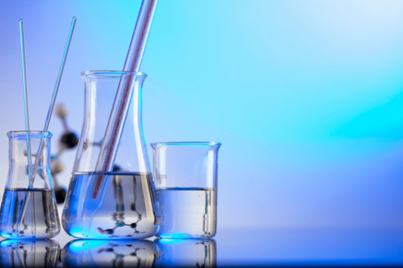 Ein paar Laborgefäße und Glasstäbe vor farbig beleuchtetem Hintergrund