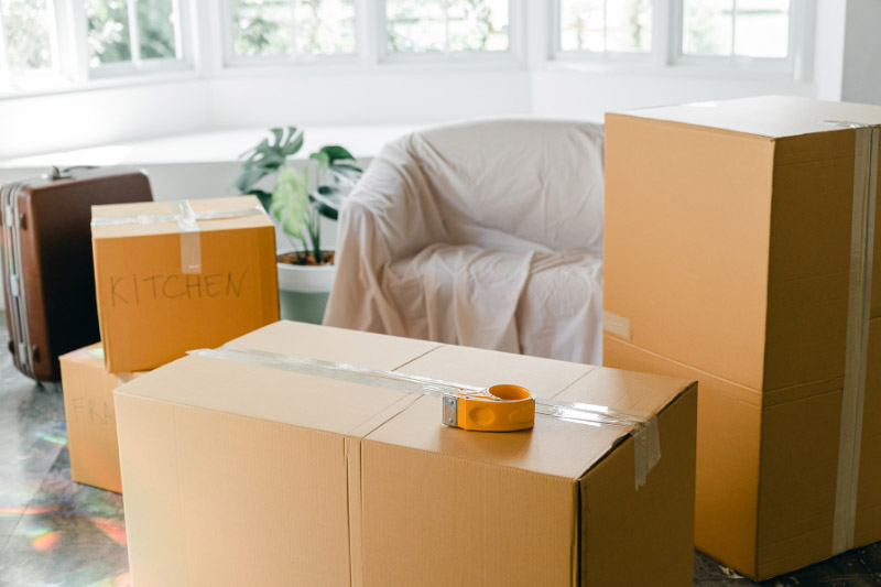 In einer leeren Wohnung ist ein Sessel abgedeckt, Koffer und beschriftete Kartons stehen herum