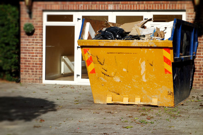 Vor einer leeren Wohnung steht ein bis oben hin gefüllter Sperrmüllcontainer