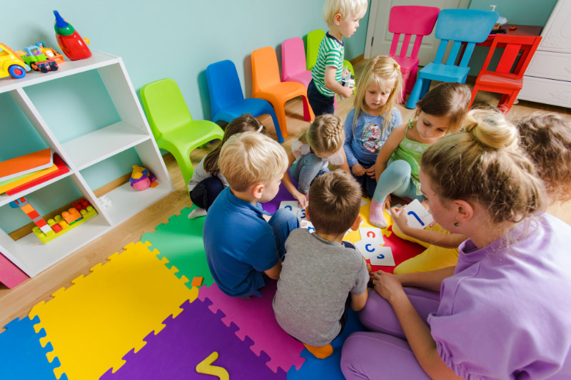 Eine Gruppe Kinder spielt im Kindergarten, wo viele farbige Bodenmatten, bunte Stühle und Spielsachen befinden