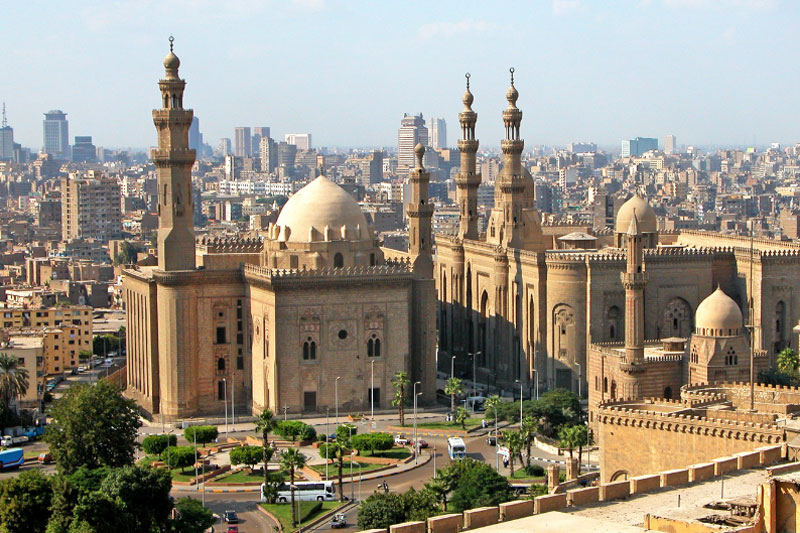 Blick auf eine alte Moschee in Ägypten und einer Stadt voller Hochhäuser im Hintergrund