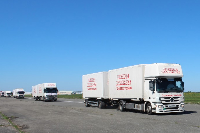 Eine Kolonne Mansholt-Umzugswagen und Transport-LKW fährt durch das Bild