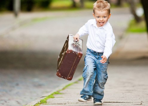Ein kleiner Junge läuft fröhlich mit einem Koffer in der Hand eine Straße entlang
