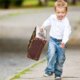 Ein kleiner Junge läuft fröhlich mit einem Koffer in der Hand eine Straße entlang