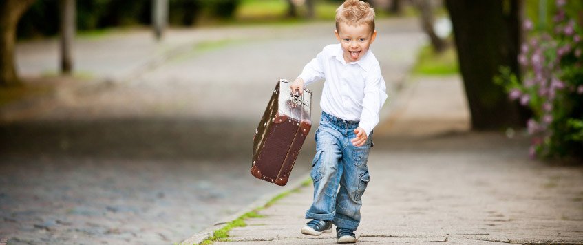 Ein kleiner Junge läuft fröhlich mit einem Koffer in der Hand eine Straße entlang
