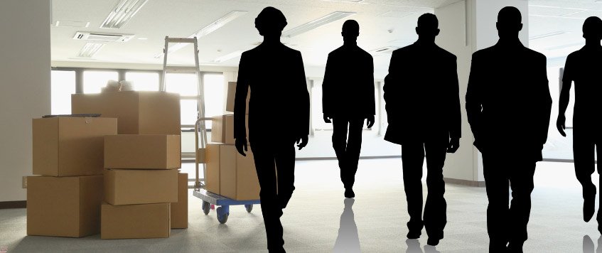 Mehrere schwarze Silhouetten gehen auf einen Stapel Umzugskartons in einem hellen Büro zu – Symbolbild für die Frage, wieviel Umzugshelfer man braucht