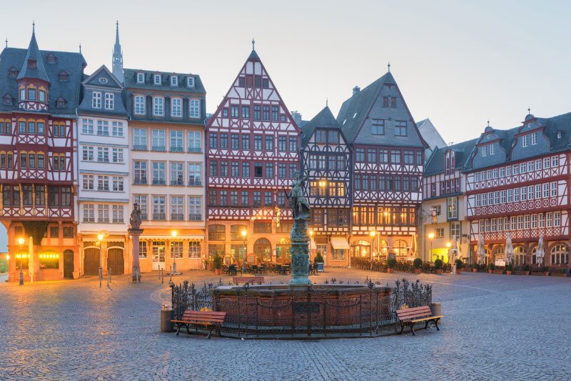 Frankfurt-2 Historischer Römerberg in Frankfurt am Main mit Fachwerkhäusern, Brunnen und beleuchtetem Marktplatz in der Dämmerung.