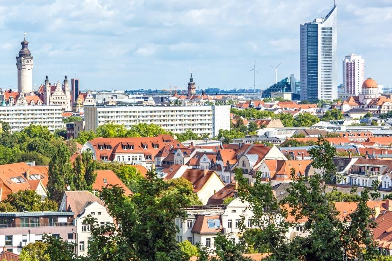 Stadtpanorama von Leipzig mit historischen Gebäuden, Wohnhäusern mit roten Dächern, Hochhäusern und Grünflächen bei schönem Wetter