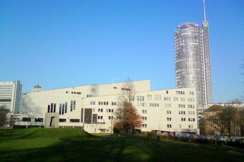 Modernes Gebäude des Museums Folkwang in Essen mit dem RWE-Turm im Hintergrund und Grünfläche im Vordergrund unter klarem Himmel