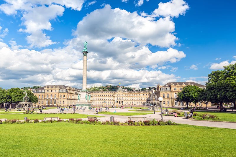 Schlossplatz in Stuttgart mit Jubiläumssäule, grüner Parkanlage und historischem Königsbau unter blauem Himmel mit Wolken
