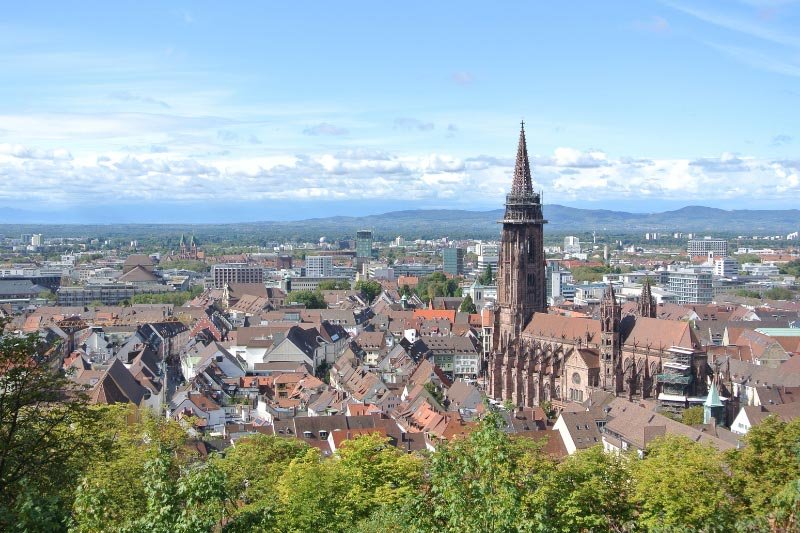 Freiburg-1 Panoramablick über Freiburg im Breisgau mit Freiburger Münster und Altstadt vor hügeliger Landschaft und blauem Himmel.