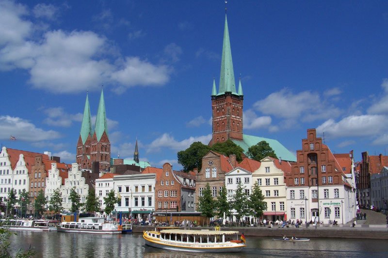 Historische Altstadt von Lübeck mit Blick auf die Marienkirche und den Dom, rote Backsteingebäude und grüne Kirchtürme entlang der Trave