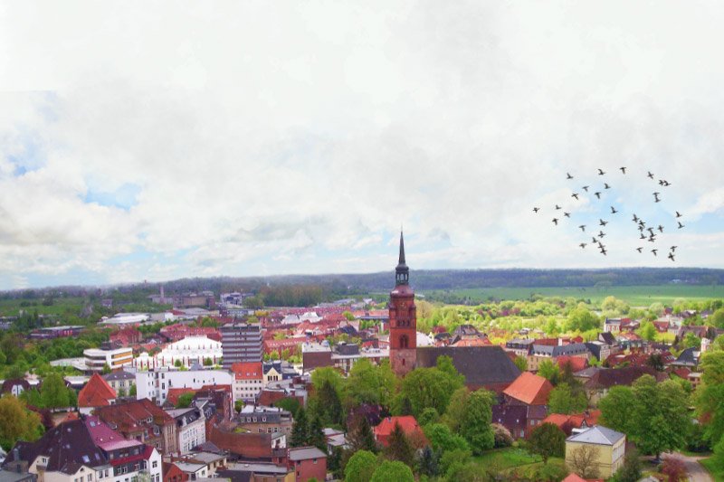 Luftaufnahme von Norderstedt mit roter Backsteinkirche und Kirchturm, umgeben von Wohnhäusern, viel Grün und einem Vogelschwarm am Himmel