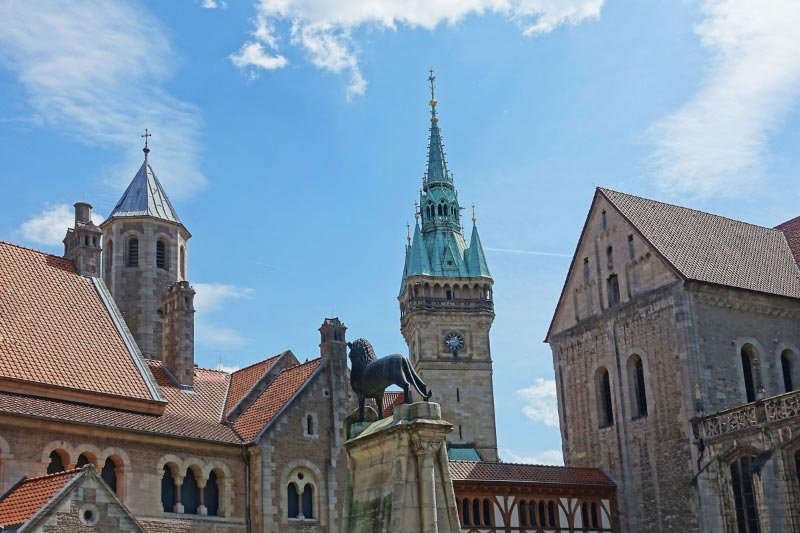Historische Gebäude rund um den Braunschweiger Dom mit Löwenstatue im Vordergrund und blauem Himmel im Hintergrund.