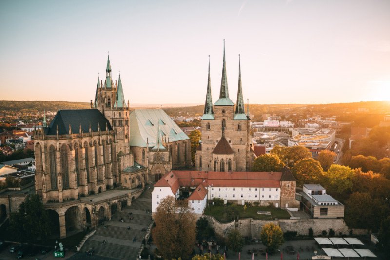 Blick auf den Erfurter Dom und die Severikirche auf dem Domberg in Erfurt bei Sonnenuntergang mit historischer Altstadt und moderner Stadtlandschaft im Hintergrund.