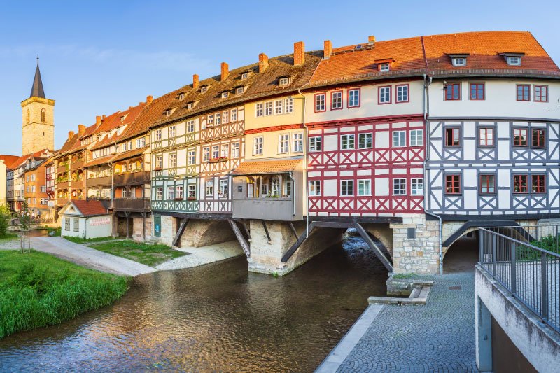 Historische Krämerbrücke in Erfurt mit farbenfrohen Fachwerkhäusern über dem Fluss Gera bei sonnigem Wetter.