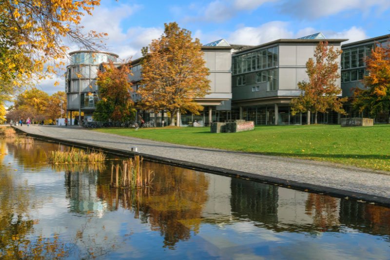 Modernes Hochschulgebäude am Wasser in Göttingen mit herbstlicher Parkanlage und spiegelnder Uferpromenade