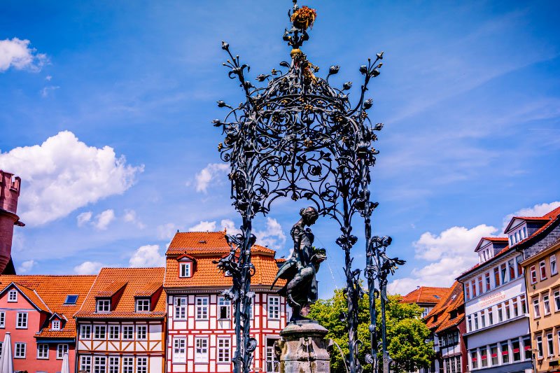 Gänseliesel-Brunnen auf dem Marktplatz in Göttingen mit kunstvoll geschmiedetem Brunnenaufbau und historischen Fachwerkhäusern im Hintergrund